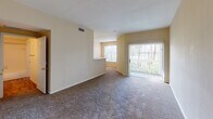 This single-story unit in Beaumont, Texas offers a well-organized layout designed for comfortable everyday living. The living area is generously proportioned, featuring neutral-toned carpet, warm beige walls, and abundant natural light streaming through a large picture window and a sliding glass door that opens to an outdoor view framed by mature trees. A half-wall peninsula separates the living space from the kitchen, adding architectural interest while maintaining an open feel.

The galley-style kitchen is efficiently designed with ample upper and lower cabinetry in a light wood finish, white countertops, hardwood-style flooring, a double basin sink, and white appliances including a range and refrigerator. A dedicated entry area with tile flooring marks the front door, transitioning smoothly into the carpeted living space.

The bedroom is a comfortable retreat with carpet flooring, a ceiling fan with light fixture, a window with outdoor views, direct bathroom access, and a reach-in closet with built-in shelving. The bathroom features hardwood-style flooring, a tub-shower combination with white tile surround, a vanity with storage cabinets above, and a light countertop. Throughout the unit, the overall ambiance is bright, clean, and functional.