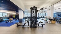 Located at 111 Towne St in Stamford, Connecticut, this professionally appointed fitness center offers a generously sized, single-floor layout designed to accommodate a comprehensive range of workout routines. The space is characterized by a modern, sophisticated aesthetic, with a bold navy and white color palette, rubber flooring throughout, and a combination of high ceilings and large windows that flood the facility with natural light and provide views to the outdoors.

The cardio zone features a row of treadmills, stair climbers, and stationary bikes aligned along the windowed perimeter, each equipped with individual screens. A dedicated strength training area includes a multi-station cable machine, Smith machine, power rack, and a full rack of Matrix dumbbells, supported by adjustable benches for versatile lifting options. A distinct functional training zone is defined by bright blue flooring and houses free weights, medicine balls, and open floor space for dynamic exercises.

Mirrored walls in the free weight section enhance the sense of depth throughout the space. Wall-mounted televisions provide entertainment options, while suspended linear lighting fixtures ensure the entire facility is well-lit. Glass-paneled interior partitions and double-door entry points contribute to an open, airy feel. The overall design balances high-performance functionality with a polished, modern ambiance.