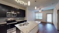Located at 2250 Sara Jane Pkwy in Grand Prairie, Texas, this single-floor residence offers a thoughtfully designed layout with contemporary finishes throughout. The kitchen serves as a central highlight, showcasing rich dark cabinetry, granite countertops, a tile backsplash, and a full suite of stainless steel appliances including a refrigerator, electric range, and built-in microwave. A kitchen island with a double stainless steel sink and pendant lighting above adds both function and style, flowing seamlessly into the open living area. The living space features hardwood-style flooring and a ceiling fan, with a large window that invites natural light and outdoor views. The bedroom is carpeted for comfort, with its own large window and ceiling fan, creating a bright and relaxing retreat. A dedicated laundry area is conveniently integrated into the unit. The bathroom features a granite-topped dark vanity with an undermount sink and a large mirror, complemented by wood-style flooring transitioning to carpet in the adjacent bedroom. Throughout the unit, neutral wall tones and consistent design elements create a cohesive, modern ambiance well-suited for comfortable everyday living.