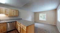 Located at 3930 NW Witham Hill Dr in Corvallis, Oregon, this single-floor unit offers a practical and comfortable layout with a variety of functional spaces throughout. The kitchen is a standout feature, outfitted with natural wood cabinetry, granite-style countertops, and a full suite of stainless steel appliances including a refrigerator, range, and dishwasher. Rich hardwood-style flooring runs through the kitchen area, adding warmth and durability. A peninsula counter connects the kitchen to the adjacent living and dining area, which transitions to soft carpet and is brightened by multiple windows offering views of surrounding greenery. The bedrooms are carpeted and well-sized, each benefiting from natural light through blinds-fitted windows. One bedroom features a ceiling fan and a spacious closet with sliding doors, while another offers baseboard heating and an exterior view. An additional room with hardwood-style flooring provides flexibility for use as a home office or storage space. The bathroom includes a vanity with matching wood cabinetry and granite-style countertop, a tiled floor, and a full shower-tub combination. Textured ceilings are consistent throughout, and the overall neutral color palette creates a clean, inviting atmosphere across the entire unit.