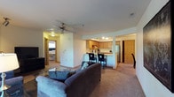 This single-floor residence offers a thoughtfully designed open-concept layout connecting the living, dining, and kitchen areas. The living room features a ceiling fan, a gas fireplace with a wood-trimmed mantel set into a built-in niche, and a sliding glass door that allows natural light and outdoor views. A glass-top coffee table and plush carpeting complete the comfortable setting.

The kitchen is well-equipped with warm oak cabinetry, stainless steel appliances including a range and refrigerator, a double sink, and wood-look flooring. A breakfast bar with bar seating connects the kitchen to the living space, while a separate dining area accommodates a four-seat glass-top table beneath a pendant light fixture.

Two bedrooms, each carpeted and featuring windows with natural light, offer closet storage and space for full or queen-sized beds. Two bathrooms are present — one with a shower/tub combination and the other with a walk-in shower — both featuring wood-look flooring and oak vanity cabinetry.

A dedicated in-unit laundry area houses a full-sized washer and dryer with overhead cabinetry, adding notable convenience to this functional and comfortable space.