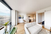 This thoughtfully designed one-bedroom, one-bathroom residence offers a clean, modern aesthetic with light hardwood flooring and crisp white walls throughout. The open-concept living, dining, and kitchen area forms the heart of the home, anchored by expansive floor-to-ceiling windows that frame sweeping city and mountain views, flooding the space with abundant natural light. The kitchen is outfitted with light wood cabinetry, white quartz countertops, a subway tile backsplash, stainless steel appliances including a gas range, and a peninsula with bar seating — ideal for casual dining. The living area provides a comfortable, well-proportioned layout with a wall-mounted media console. The bedroom is a serene retreat with light-toned walls, hardwood flooring, and access to a dedicated walk-in closet with built-in shelving. A second closet in the hallway provides additional storage. The bathroom features large-format tile flooring, a glass-enclosed walk-in shower with textured tile surround, and a floating wood vanity with a white countertop and integrated sink. Two hallways connect the rooms efficiently, completing this well-appointed, contemporary residence.