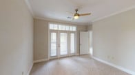 This single-floor, 2-bedroom, 2-bathroom residence offers a thoughtfully designed layout with a cohesive neutral color palette and quality finishes throughout. The main living area features plush carpeting, crown molding, and a ceiling fan, with French-style doors topped by transom windows that flood the space with natural light and provide access to an outdoor balcony. The kitchen is a standout, showcasing rich dark cabinetry, granite countertops, a stone tile backsplash, dark wood-look tile flooring, and a full suite of black appliances including a gas range, microwave, and stainless steel refrigerator. Both bedrooms are generously proportioned with soft carpet flooring. The primary bedroom features French doors with transom windows and direct balcony access, while the second bedroom benefits from multiple windows offering views of the surrounding greenery. A walk-in closet with wire shelving provides ample storage. The primary bathroom includes dark cabinetry with granite countertops and dark tile flooring, while the second bathroom offers a soaking tub with white tile surround and light tile flooring. Track lighting and a spacious open layout further enhance the functional and comfortable character of this well-appointed home.