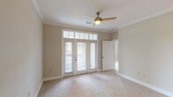 This single-floor, 2-bedroom, 2-bathroom residence offers a thoughtfully designed layout with a cohesive neutral color palette and quality finishes throughout. The main living area features plush carpeting, crown molding, and a ceiling fan, with French-style doors topped by transom windows that flood the space with natural light and provide access to an outdoor balcony. The kitchen is a standout, showcasing rich dark cabinetry, granite countertops, a stone tile backsplash, dark wood-look tile flooring, and a full suite of black appliances including a gas range, microwave, and stainless steel refrigerator. Both bedrooms are generously proportioned with soft carpet flooring. The primary bedroom features French doors with transom windows and direct balcony access, while the second bedroom benefits from multiple windows offering views of the surrounding greenery. A walk-in closet with wire shelving provides ample storage. The primary bathroom includes dark cabinetry with granite countertops and dark tile flooring, while the second bathroom offers a soaking tub with white tile surround and light tile flooring. Track lighting and a spacious open layout further enhance the functional and comfortable character of this well-appointed home.