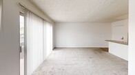 Located at 20939 Parthenia St in Canoga Park, California, Unit 213 is a thoughtfully laid-out studio that maximizes its compact footprint across a single floor. The open-concept living area features light gray carpeting, white walls, and a textured ceiling, creating a clean, neutral aesthetic throughout. Large vertical-blind-covered sliding glass doors and an adjacent window flood the space with natural light while providing outdoor views and access, with a wall-mounted AC unit conveniently positioned nearby.

The kitchen connects seamlessly to the living area via a peninsula counter finished with speckled granite-style laminate, offering additional prep and casual dining space. White cabinetry lines the walls above and below, complemented by a white electric range and refrigerator. Wood-look flooring in the kitchen adds a subtle contrast to the carpeted living space.

The bathroom maintains the same cohesive design language, featuring a wide granite-style vanity countertop with an undermount sink, white cabinetry with brushed nickel hardware, a large mirror, a multi-globe light fixture, and wood-look flooring. A dedicated closet provides practical storage. Overall, the unit offers a bright, functional living environment with consistent finishes throughout.