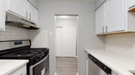 This single-floor residence offers a thoughtfully updated interior with a cohesive, neutral color palette and modern finishes throughout. The galley-style kitchen is a standout feature, equipped with white shaker cabinetry fitted with brushed nickel hardware, white quartz countertops, a classic subway tile backsplash, and a full suite of stainless steel appliances including a gas range, dishwasher, and refrigerator. Durable luxury vinyl plank flooring runs through the kitchen, hallway, and main living area, providing a clean and contemporary look that is easy to maintain. The living area is open and well-proportioned, with crisp white trim and a door leading to additional rooms. The bedrooms are finished with plush carpet and feature built-in closet space, with windows dressed in blinds that allow for natural light and privacy. A hallway closet with sliding panel doors provides convenient additional storage. The bathroom is finished with clean white tile work, a full soaking tub with a tub-surround, and a tile accent wall. The overall ambiance of the space is bright, fresh, and move-in ready, with consistent modern updates visible in every room.