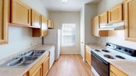 This single-floor residence offers a well-organized and functional layout designed for comfortable everyday living. The open living area is carpeted and bathed in natural light, with a pendant light fixture overhead and direct access to an outdoor patio through a glass door, providing a seamless connection to the exterior. Adjacent to the living space, the galley-style kitchen is efficiently designed with warm honey-toned cabinetry lining both walls, light countertops, a double-basin sink, and standard appliances including an electric range and refrigerator. A window at the end of the kitchen allows additional natural light to fill the space. The bedrooms are carpeted and feature ceiling fans with light kits, multiple windows fitted with blinds, and ample closet space — one bedroom notably includes two closets and an adjoining bathroom with a vanity and soaking tub. A second full bathroom offers a tub-shower combination, wood-look flooring, and matching cabinetry. Throughout the unit, the neutral color palette, consistent flooring materials, and clean white walls create a bright, cohesive ambiance that is both practical and easy to personalize.