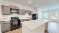 Located at 4029 Flat Shoals Pkwy in Decatur, GA, this one-bedroom, one-bathroom unit offers a well-designed single-floor layout that maximizes its compact footprint. The open-concept living and kitchen area is anchored by a striking white kitchen island that doubles as additional counter and prep space. The kitchen is outfitted with taupe shaker-style cabinetry, light quartz-style countertops, and a full suite of black appliances including a range, over-the-range microwave, dishwasher, and refrigerator. Recessed lighting and light hardwood-style flooring throughout the main living area contribute to a bright, clean aesthetic. The bedroom is comfortably sized, featuring soft wall-to-wall carpet, a ceiling fan, and a window with blinds that allows natural light and outdoor views. The bathroom connects directly to a dedicated closet with wire shelving, offering practical storage. The bathroom itself includes a vanity with cabinetry and a standalone shower. Clean white walls throughout the unit create a neutral, move-in-ready canvas. The overall design is modern and functional, well-suited for comfortable single-occupant or couple living in the Decatur area.