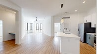 This single-floor residence showcases a clean, modern design characterized by crisp white walls, light wood-tone flooring, and an open-concept floor plan that promotes a seamless flow between living spaces. The expansive living area benefits from large floor-to-ceiling windows and glass doors that flood the space with natural light, complemented by a ceiling fan overhead.

The kitchen is a standout feature, equipped with stainless steel appliances including a French door refrigerator, electric range, and microwave. A two-tone cabinetry scheme pairs white upper cabinets with grey lower cabinets, accented by a white subway tile backsplash and light quartz countertops. A generously sized island with an undermount sink and matte black faucet serves as a central gathering point, illuminated by pendant lighting above.

The bedrooms offer elevated ceilings, ceiling fans, and natural light from well-positioned windows. Bedroom closets feature panel doors with matte black hardware. The bathrooms maintain the home's contemporary aesthetic, with one featuring a tiled tub-shower combination and matte black fixtures, and another offering a glass-enclosed walk-in shower, both with grey floating vanities and white quartz countertops.