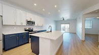 Located in Phoenix, AZ, this well-designed single-floor residence offers a thoughtful layout encompassing a kitchen, living room, bedroom, bathroom, closet, and dedicated laundry room. The open-concept kitchen is a standout feature, showcasing a striking two-tone design with crisp white upper cabinetry and deep navy lower cabinets, both accented with gold hardware. A large central island with a white quartz countertop and matte black sink serves as the focal point, complemented by a white subway tile backsplash and stainless steel appliances. The kitchen flows seamlessly into the bright living area, which is finished with light wood-look flooring found throughout the entire unit and a ceiling fan overhead. Sliding glass doors open to a private balcony, filling the living space with natural light. The bedroom is a comfortable, well-proportioned retreat featuring a ceiling fan, a window with blinds, and the same warm wood-look flooring. The full bathroom includes a soaking tub with a tiled surround, matte black fixtures, and direct access to a dedicated walk-in closet with built-in shelving and hanging rods. A separate laundry room with a full-size washer and dryer completes this efficiently designed home.