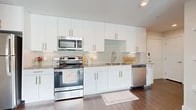 This thoughtfully laid-out one-bedroom, one-bathroom residence makes excellent use of its space across a single floor. Warm hardwood-style flooring flows continuously throughout every room, creating a cohesive and inviting atmosphere.

The galley-style kitchen is a standout feature, finished with crisp white cabinetry accented by gold-toned hardware and extending floor to ceiling for generous storage. Granite countertops provide a durable and stylish work surface, while a textured glass tile backsplash in soft seafoam tones adds a refined decorative touch. A full suite of stainless steel appliances — including a range, over-the-range microwave, dishwasher, and refrigerator — completes this functional and attractive kitchen.

The bedroom is a calm, light-filled retreat with neutral walls, a ceiling fan, and a window offering views of the surrounding greenery and cityscape. A large built-in closet with paneled double doors provides ample storage.

The bathroom mirrors the kitchen's design sensibility, featuring a granite-topped white vanity with gold hardware, a large mirror, and a shower-tub combination. The entrance welcomes residents with a sense of openness, anchored by a set of paneled double doors that add architectural character to the space.
