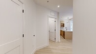 Located at 65 Jolley Dr in Bloomfield, Connecticut, this thoughtfully designed single-floor residence combines modern finishes with warm architectural details. Light-toned hardwood flooring flows throughout the main living areas, complemented by crisp white walls and black hardware accents that lend a contemporary edge. The open living area is distinguished by exposed natural wood ceiling beams and recessed lighting, creating an inviting atmosphere. Sliding glass doors lead to a private outdoor balcony with views of surrounding autumn foliage, filling the space with natural light. The kitchen is well-appointed with light wood cabinetry, white quartz countertops, a tiled backsplash, stainless steel appliances including a refrigerator, range, and microwave, and a peninsula with an undermount sink and matte black faucet. Bedrooms are finished with plush carpeting; one features a built-in closet with shelving and a sliding panel door, while another offers dual windows overlooking lush greenery. The bathroom showcases dramatic dark marble-look tile flooring, a floating wood vanity with white countertop, an oval black-framed mirror, and a glass-enclosed shower. A dedicated laundry area houses a full-size Samsung washer and dryer. The hallway connects all spaces efficiently, completing this refined and functional layout.