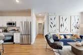 Located in Aurora, CO, this well-appointed one-bedroom, one-bathroom residence offers a thoughtfully designed open-concept layout across a single floor. The combined kitchen and living area serves as the heart of the home, featuring light wood-tone flooring that flows seamlessly throughout. The kitchen is outfitted with full-height white shaker cabinets, granite-style countertops, stainless steel appliances including a refrigerator, range, microwave, and dishwasher, and open display shelving. A round dining table with bar-height seating provides a casual dining area adjacent to the kitchen. The living room is distinguished by a bold teal accent wall, large windows that invite natural light, and a hallway leading to the private quarters. The bedroom is a comfortable retreat featuring plush carpet, a ceiling fan, a teal accent wall, natural light from a large window, and space for a dedicated work area. A walk-in closet offers organized storage. The bathroom includes a granite-topped white vanity, wood-tone flooring, and a full tub-shower combination. Recessed lighting throughout adds a clean, contemporary finish to this efficient and stylish Aurora residence.