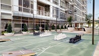 This dynamic outdoor amenity space is nestled within a contemporary urban high-rise development, offering a well-appointed courtyard environment designed for recreation and socializing. At its center lies a spacious multi-use game court finished in green modular sport surfacing, marked with shuffleboard lanes and accompanied by oversized chess sets and cornhole boards, providing a variety of engaging activities for residents or guests.

The courtyard is framed by the building's striking glass curtain wall façade, which floods the surrounding walkways with natural light and creates a seamless visual connection between interior and exterior spaces. Large, sculptural white planters filled with manicured topiaries and ornamental trees are thoughtfully arranged throughout, introducing lush greenery that softens the urban environment and adds a refined aesthetic.

String lights are strung overhead across the courtyard, lending a warm, inviting ambiance during evening hours. A pergola-covered terrace runs along one side of the space, offering shaded seating with wicker furnishings and open views of the surrounding city skyline. Travertine-style pavers line the perimeter walkways, contributing to the elevated, polished character of the space.

Raised planter beds with mature trees and layered plantings further define zones within the amenity area, while the building's upper-floor balconies overlook the courtyard below, reinforcing the sense of community and connectivity throughout this well-designed outdoor retreat.