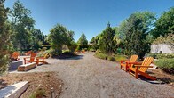 Located at 6245 Willow Ln in Boulder, Colorado, this generously sized single-level outdoor space offers a thoughtfully designed landscape experience. Gravel pathways wind throughout the grounds, connecting a series of distinct gathering areas framed by lush, layered plantings of ornamental grasses, native shrubs, perennials, and mature evergreen and deciduous trees.

Multiple fire pit seating areas are positioned throughout the space, each furnished with vibrant orange Adirondack chairs that invite relaxed conversation and outdoor enjoyment. Natural boulder accents are integrated into the planted beds, reinforcing the Colorado aesthetic and providing informal additional seating.

A standout feature is the outdoor kitchen and dining area, anchored by a handsome wood-and-stone pergola. The built-in grill station and bar-height seating make it well-suited for entertaining and communal gatherings. A welcoming entry pergola with stone pillars marks the main arrival point from the adjacent parking area, setting the tone for the natural, Colorado-inspired atmosphere throughout.

Lush green lawn areas border portions of the space, adding softness alongside the gravel surfaces. Under the wide-open Boulder sky, the grounds benefit from abundant natural light and clear views of the surrounding tree canopy, creating an inviting, park-like setting ideal for community gathering and outdoor leisure.