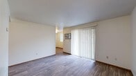 This single-floor unit offers a practical and comfortable layout across several distinct living spaces. The living area is a standout feature, showcasing durable hardwood-style flooring and a full-length sliding glass door dressed with vertical blinds that flood the space with natural light. A wall-mounted air conditioning unit ensures year-round comfort. An adjacent area with matching flooring provides additional flexible living or dining space, complete with a floor vent for climate control.

The kitchen is efficiently designed with ample cabinetry featuring warm wood-toned accents, a double-basin sink, a dishwasher, a range, and a full-size refrigerator, all complemented by hardwood-style flooring. A hallway connects the main living spaces to the bedrooms, where plush neutral carpeting creates a cozy atmosphere. Each bedroom benefits from natural light through slatted blinds and ceiling fans with integrated lighting. Closet space is provided via sliding-panel doors.

The bathroom is clean and functional, featuring a shower/tub combination, toilet, vanity with storage, and hardwood-style flooring. Throughout the unit, neutral wall tones and wood-trimmed doors and baseboards create a cohesive, understated aesthetic that is move-in ready.