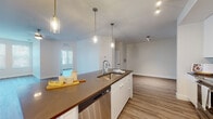 Located at 4950 W Prescott St in Tampa, Florida, this modern single-story residence showcases a clean, contemporary design with an open-concept floor plan and consistent wood-look flooring throughout. The kitchen serves as a central highlight, featuring a large island with a dark countertop, white cabinetry, a white subway tile backsplash, and a full suite of stainless steel appliances including a French door refrigerator, electric range, over-the-range microwave, and dishwasher. Pendant lighting with brass accents illuminates the island, adding warmth to the space. The kitchen flows seamlessly into the living area, which is bright and airy, benefiting from natural light through multiple windows fitted with plantation-style blinds. Ceiling fans with integrated lighting are present in the bedrooms and living areas, promoting comfort and airflow. The bedrooms offer a clean, neutral palette with ample natural light and views of the surrounding neighborhood. The bathrooms are elegantly appointed with LED-backlit vanity mirrors, undermount sinks, and dark or white cabinetry. One bathroom features a sleek frameless glass walk-in shower with large-format tile surround. An in-unit laundry area is also visible, adding everyday convenience to this well-designed Tampa residence.