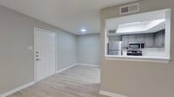 This single-floor unit presents a clean, modern aesthetic throughout its thoughtfully arranged layout. The main living area is open and airy, finished with light wood-style laminate flooring and neutral gray walls that create a bright, cohesive atmosphere. A ceiling fan with integrated lighting serves the space, while a window fitted with blinds allows for natural light and privacy control. The entry foyer flows directly into the living area, maintaining a seamless and functional transition.

The kitchen is positioned adjacent to the living space via a pass-through opening, providing visual connectivity. It features gray cabinetry, stainless steel appliances including a refrigerator, range, microwave, and dishwasher, along with a built-in overhead fluorescent light fixture that illuminates the workspace effectively.

The bedroom is carpeted for added comfort, with a window offering natural light and a closet accessible via a private door. The bathroom is finished with large-format gray tile surrounding the tub-shower combination, complemented by a white vanity with a light countertop, wood-style flooring, and brushed nickel fixtures and hardware throughout, contributing to the unit's consistently modern and neutral design language.