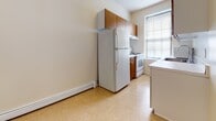 Located at 406 Prospect Ave in Hackensack, New Jersey, this single-floor residence offers a practical and comfortable layout with well-defined living spaces. The kitchen is efficiently designed, featuring warm wood-toned cabinetry, a full-size refrigerator, an electric range, and a stainless steel sink. Light-toned vinyl tile flooring and a window with blinds allow natural light to brighten the space, while a baseboard heating unit ensures year-round comfort. The living area is generously proportioned, with neutral-toned wall-to-wall carpeting, cream-colored walls, and a baseboard heating system. A closeted storage area is accessible from this room, adding practical functionality. The bedroom mirrors this clean aesthetic, offering soft carpeting, a large window that invites natural light, and baseboard heating. The bathroom is finished in crisp white subway tile from floor to ceiling, complemented by large-format white floor tiles. It includes a single-basin vanity, a full soaking tub with a showerhead, and a multi-pane window that provides ventilation and light. The overall ambiance of the space is clean, understated, and move-in ready, with consistent neutral tones and functional finishes throughout.