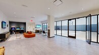 Located at 570 North 5th Street in Philadelphia's vibrant Northern Liberties neighborhood, this single-floor amenity facility offers an impressive range of recreational and social spaces across a generously sized footprint. The centerpiece is a full-size indoor basketball court, finished with polished hardwood flooring, regulation court markings, and wall-mounted basketball hoops. Padded wall panels line the court perimeter for safety, while high exposed ceilings with industrial-style lighting create an energetic, open atmosphere. The court also accommodates volleyball, as evidenced by the portable net and multi-sport line markings.

Adjacent to the court, large floor-to-ceiling glass walls and wide sliding glass doors connect the interior lounge area to the court, flooding the space with natural light and providing seamless sightlines. The lounge is stylishly appointed with bold orange curved seating, wall-mounted flat-screen TVs, warm textured wall panels, and curated artwork. A casual dining and gaming zone features arcade machines, additional screens, and bistro-style seating.

A dedicated fitness studio with wood-look flooring and glass partition walls offers a clean, modern environment for group exercise. Light tile flooring flows throughout the common areas, tying the entire space together with a contemporary, cohesive aesthetic.