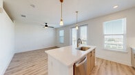 Located in Farmers Branch, Texas, this thoughtfully designed 2-bedroom, 1-bathroom residence offers a clean, modern aesthetic across a single floor. Light wood-style flooring runs seamlessly throughout, creating a cohesive and airy feel in every room. The open-concept kitchen and living area serves as the heart of the home, showcasing light wood cabinetry, a subway tile backsplash, stainless steel appliances including a French door refrigerator and electric range, and a striking quartz island with an undermount sink and gold-accented faucet. Pendant lighting adds a stylish touch above the island, while a window brings in natural light. Both bedrooms are well-proportioned, with crisp white walls, ceiling fans, and ample natural light — the primary bedroom features windows on two sides, including access to a balcony. The bathroom continues the modern design language with light wood vanity cabinetry, quartz countertops, a large gold-framed mirror, and matte black hardware accents. A dedicated closet provides practical storage. The overall ambiance is fresh, bright, and move-in ready, reflecting contemporary residential design.