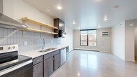 This studio unit at 310 Main Ave in Fargo, North Dakota, presents a thoughtfully designed open-concept layout that maximizes every square foot. The polished aggregate concrete flooring runs throughout the entire unit, lending a clean, modern aesthetic that ties the space together cohesively.

The kitchen is a standout feature, outfitted with dark-toned cabinetry, white countertops, and a classic subway tile backsplash. Stainless steel appliances — including a refrigerator, electric range with a wall-mounted range hood, dishwasher, and built-in microwave — provide a fully functional cooking space. Open natural wood floating shelves add both storage and visual warmth to the kitchen wall.

The main living area is bright and open, benefiting from a large picture window that invites natural light and offers views of the surrounding streetscape. A wall-mounted air conditioning unit and baseboard heating ensure year-round climate comfort. A dedicated closet with a hanging rod provides practical storage off the main living space.

The bathroom features a combined tub and shower enclosure, a toilet, and polished aggregate flooring consistent with the rest of the unit, maintaining a unified design throughout. The overall ambiance of the unit is clean, contemporary, and efficiently organized.