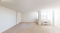 Located at 3701 Conshohocken Ave in Philadelphia, PA, this efficiently designed single-floor unit offers a clean, neutral aesthetic throughout. The open living area is finished with wall-to-wall beige carpeting and bright white walls, creating a light and airy atmosphere. A large window fitted with vertical blinds allows natural light to fill the space, while a wall-mounted HVAC unit provides climate control. The layout flows naturally from the living area toward the entryway, which features a dedicated closet for additional storage. The kitchen is well-appointed with white cabinetry extending to the ceiling, offering generous storage capacity. Dark laminate countertops provide a contrasting work surface, and the kitchen is equipped with a white gas range, an overhead ventilation hood, and a stainless steel sink. The full bathroom is finished with light tile flooring and white walls, and includes a toilet and a standard soaking tub with a shower rod. The overall design of the unit is clean and functional, with a consistent white palette that enhances the sense of space and keeps the interior feeling open and manageable throughout.
