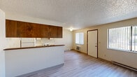 Located at 1026 E 30th Ave in Spokane, WA, this one-bedroom, one-bathroom unit offers a practical and functional layout across a single floor. The open-concept kitchen and living area serves as the heart of the unit, featuring light wood-style vinyl flooring, a textured ceiling, and a window that allows natural light to fill the space. The kitchen is equipped with white appliances including a coil-top electric range and a full-size refrigerator, complemented by a mix of white and warm wood-toned cabinetry providing ample storage. A wall-unit air conditioner and baseboard heaters are present throughout for year-round climate control. The living area offers generous open space with neutral wall tones and direct access to the entry door. A hallway connects the main living space to the private bedroom, which is carpeted and features a large sliding wood-panel closet door and a window with vertical blinds that brings in natural light. The full bathroom includes a tiled tub-and-shower combination with accessibility grab bars and baseboard heating. The unit's straightforward layout, consistent neutral palette, and functional features make it a well-organized and comfortable living space.