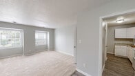 Located at 600 Ashbrook Ct in Fayetteville, North Carolina, this single-story residence offers a clean, neutral aesthetic with a practical and well-organized layout. The interior is finished with soft, light gray walls and crisp white trim throughout, creating a bright and cohesive atmosphere across every room.

The living area is generously proportioned, featuring plush wall-to-wall carpeting and dual windows that invite natural light deep into the space. The kitchen is well-appointed with white cabinetry, granite-look countertops, a stainless steel sink, and included appliances such as an electric range and over-the-range microwave. Wood-look flooring in the kitchen and entry areas adds a durable, stylish contrast to the carpeted rooms.

Multiple bedrooms are present throughout the home, each carpeted and equipped with ceiling fans, ample windows for natural light, and easy access to closet space. One bedroom offers a walk-in closet, while another features a pendant light fixture and direct hallway access. The bathrooms include a tub-shower combination with tiled surrounds and wood-look flooring, providing a clean and functional finish. A walk-in closet adjacent to one bath adds additional storage convenience. The home's straightforward single-floor plan ensures accessibility and ease of movement throughout.