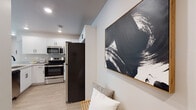 This single-floor space offers a thoughtfully designed layout that balances modern aesthetics with functional living. The kitchen is a standout feature, equipped with stainless steel appliances including a French door refrigerator, electric range, and over-the-range microwave. White shaker-style cabinetry with black hardware lines the walls, complemented by light quartz countertops and light wood-look flooring that extends throughout the common areas, creating a clean, cohesive look.

The living area is bright and welcoming, featuring recessed lighting, neutral walls, and a window that allows natural light to filter in. Bold abstract artwork adds a contemporary touch to the space. The bedrooms are carpeted for comfort, each receiving natural light through blinds-covered windows, and offer adequate space for furnishings.

Two bathrooms serve the unit, each finished with wood-look flooring, white vanities with quartz countertops, and striking matte black fixtures. One bathroom features a tub-shower combination with sliding glass doors, while the other offers a walk-in shower with a frameless black-trimmed glass enclosure. The overall design is modern and consistent, with a neutral palette accented by bold black hardware throughout.