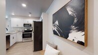 This single-floor space offers a thoughtfully designed layout that balances modern aesthetics with functional living. The kitchen is a standout feature, equipped with stainless steel appliances including a French door refrigerator, electric range, and over-the-range microwave. White shaker-style cabinetry with black hardware lines the walls, complemented by light quartz countertops and light wood-look flooring that extends throughout the common areas, creating a clean, cohesive look.

The living area is bright and welcoming, featuring recessed lighting, neutral walls, and a window that allows natural light to filter in. Bold abstract artwork adds a contemporary touch to the space. The bedrooms are carpeted for comfort, each receiving natural light through blinds-covered windows, and offer adequate space for furnishings.

Two bathrooms serve the unit, each finished with wood-look flooring, white vanities with quartz countertops, and striking matte black fixtures. One bathroom features a tub-shower combination with sliding glass doors, while the other offers a walk-in shower with a frameless black-trimmed glass enclosure. The overall design is modern and consistent, with a neutral palette accented by bold black hardware throughout.
