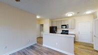 Located at 2200 Bellamy Dr in Greenville, NC, this single-floor unit offers a thoughtfully designed layout with consistent wood-look flooring and a warm, neutral color palette throughout. The open-concept kitchen serves as a central feature, equipped with gray shaker-style cabinetry extending to the ceiling, a marble-style peninsula countertop, and a full suite of black appliances including a refrigerator, range, and over-the-range microwave. The kitchen flows seamlessly into the living area, creating a spacious, connected feel. A dedicated laundry closet with washer and dryer connections is conveniently accessible just off the kitchen. The bedrooms are well-proportioned, each benefiting from natural light through blinds-fitted windows and ceiling fans for added comfort. Closet space is provided in the bedrooms, with one featuring a reach-in closet with a rod and shelf system. The bathrooms are finished with a tub-shower combination, a clean vanity with a light countertop, and neutral tile flooring. Textured ceilings and clean white trim complete the interior throughout. The unit presents a functional, move-in ready layout suited for comfortable everyday living in Greenville.