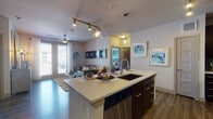 This single-floor residence is thoughtfully designed with a modern aesthetic, combining functionality and style across its well-appointed spaces. The open-concept kitchen and living area serves as the heart of the home, where rich dark-cabinetry kitchen seamlessly integrates with the main living space. The kitchen is outfitted with stainless steel appliances, a tile backsplash, quartz countertops, and a central island with bar seating, illuminated by a combination of track lighting and pendant fixtures. Wood-look flooring runs throughout the main living areas, adding warmth and continuity.

The living room offers a comfortable, inviting atmosphere with a ceiling fan, neutral wall tones, and large glass doors that open to a private balcony, allowing natural light to fill the space.

Two well-sized bedrooms feature plush carpeting and large windows dressed with sheer curtains, lending a bright, airy feel. Each bedroom connects to its own bathroom. The primary bathroom includes a walk-in glass shower, dark vanity cabinetry with quartz countertops, and large-format tile flooring. The secondary bathroom mirrors similar finishes and includes a soaking tub. Additional storage is provided throughout, including a double-door closet near the kitchen.