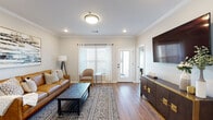 This single-story, two-bedroom, two-bathroom unit in Jonesboro, Arkansas, offers a thoughtfully designed layout with modern finishes and a cohesive aesthetic throughout. Rich hardwood-style flooring runs continuously across all rooms, anchoring the warm, contemporary design.

The living area features crown molding, recessed lighting, and a flush ceiling fixture, creating a polished atmosphere. Natural light enters through large windows dressed with blinds and sheer curtains, while a glass-paned exterior door provides direct outdoor access. A dark wood media console with gold hardware serves as a focal point opposite the seating area.

The kitchen is equipped with white shaker cabinetry, stainless steel appliances, and a spacious island with a white quartz countertop, double sink, and bar seating. An adjacent dining area is defined by crown molding and a multi-arm chandelier overhead.

Both bedrooms are comfortably sized with ceiling fans, natural light, and wall-mounted televisions. The primary bathroom features an extended white vanity, dark-framed mirror, and a separate water closet. The secondary bathroom includes a full tub-shower combination, white vanity cabinetry, and matte black hardware and fixtures throughout.