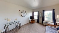 Located at 160 Sinclair St in Reno, Nevada, this single-floor studio offers a thoughtfully organized layout that makes efficient use of its space. The main living area is carpeted and filled with natural light streaming through two windows dressed with navy blue curtain panels, creating a warm and inviting atmosphere. A wall-mounted HVAC unit ensures year-round climate comfort, while the open floor plan allows for flexible furniture arrangements to accommodate both living and sleeping needs.

The sleeping area is situated near a built-in open closet with overhead shelving, providing convenient storage solutions. A partial wall partition subtly separates the sleeping zone from the entryway, which features durable tile flooring and an electrical panel neatly recessed into the wall.

The kitchenette is compact yet functional, outfitted with light-colored laminate countertops, white cabinetry above and below, and a stainless steel sink. A wall-mounted cabinet offers additional storage, keeping essentials within easy reach.

The bathroom includes a full bathtub and shower combination with clean white surroundings, a toilet, and space for supplemental storage. The overall aesthetic throughout the unit is clean and neutral, with white walls and simple finishes that provide a versatile backdrop suited to a variety of personal styles.