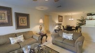 Located at 350 Byram Drive in Byram, Mississippi, this single-story residence offers a welcoming interior designed with a traditional aesthetic. The open-concept layout seamlessly connects the living room and dining area, creating a spacious and cohesive flow throughout the main living spaces. The living room is furnished with plush, neutral-toned sofas accented by decorative throw pillows, anchored by a patterned area rug and a glass-topped coffee table. A classic side table with an ornate base and a tall table lamp adds a refined touch, while framed wall art contributes warmth and character to the space. Visible wall vents indicate a central HVAC system throughout. The adjoining dining area is illuminated by an elegant chandelier, casting a warm glow over the dining table and dark upholstered chairs, making it well-suited for both everyday meals and entertaining. The light-colored flooring enhances the brightness of the interior, and the neutral wall tones provide a versatile backdrop. Overall, the home presents a comfortable, traditionally styled living environment with practical and cohesive design elements throughout.