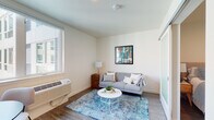 This thoughtfully designed single-floor unit offers a clean, contemporary aesthetic throughout, with light wood-tone flooring and crisp white walls creating a bright, cohesive atmosphere. The galley-style kitchen is a standout feature, outfitted with stainless steel appliances including a French door refrigerator and electric range, a built-in microwave, and a striking matte black faucet over a stainless steel sink. Marble-veined quartz countertops pair elegantly with a white subway tile backsplash and warm wood cabinetry accented with gold hardware, lending a refined, modern touch. The kitchen flows naturally toward the dining and living areas, where natural light filters in through windows, creating an airy, welcoming ambiance. The living room accommodates comfortable seating and features hardwood-style flooring, with views to the outdoors enhancing the sense of openness. The bedroom is a restful retreat, offering a well-sized sleeping area and a sliding-door closet with built-in shelving. The full bathroom is finished with a light wood vanity topped with stone counters, gold bar pulls, a black-framed mirror, and a combination tub and shower — all contributing to a spa-like, modern feel. Overall, the unit presents a well-balanced blend of functionality and contemporary design.