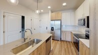 This single-floor space showcases a clean, modern design characterized by a neutral palette and thoughtful finishes throughout. The kitchen serves as a central highlight, featuring two-tone cabinetry that pairs white upper cabinets with warm wood-toned lower cabinets, light quartz countertops, and a full suite of stainless steel appliances including a French door refrigerator, electric range, over-the-range microwave, and dishwasher. A peninsula with an undermount sink and a globe pendant light overhead adds both functionality and style, while light wood-look flooring and a subway tile backsplash complete the contemporary aesthetic.

The bedrooms are carpeted and bright, each benefiting from large windows fitted with horizontal blinds that invite natural light and offer views of the surrounding exterior. The space includes two bathrooms: a full bathroom with a soaking tub, single-sink vanity with white cabinetry, and wood-look flooring, and a second bathroom featuring a glass-enclosed walk-in shower, an elongated single-sink vanity, and direct access to an adjoining bedroom. Throughout the unit, recessed lighting, clean white walls, and consistent flooring choices create a cohesive and welcoming atmosphere.