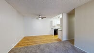 Located at 21701 Foothill Blvd in Hayward, California, this single-floor unit offers a practical and well-organized layout. The open living and dining area features a combination of warm hardwood flooring and plush carpet, with a ceiling fan overhead and a textured ceiling throughout. The space flows directly into a galley-style kitchen equipped with white cabinetry, gray laminate countertops, a black refrigerator, an electric range, and a dishwasher — all set atop rich hardwood floors with ample upper and lower cabinet storage on both sides.

The bedrooms are carpeted for comfort, each benefiting from natural light through windows with outdoor views of surrounding greenery. One bedroom includes a dedicated walk-in closet as well as an additional door for extra storage, while a baseboard heater provides supplemental warmth. A wall-mounted AC unit is also present in the main living area for climate control.

The full bathroom features a white vanity with a gray countertop, a single-sink setup, and a shower-tub combination with a curtain enclosure, finished with hardwood flooring. The textured ceilings are consistent throughout the unit, contributing to a cohesive aesthetic. Overall, the space is clean, functional, and well-lit, offering comfortable single-floor living.