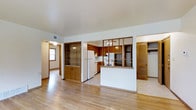 This single-floor residence offers a practical and well-organized layout designed for comfortable everyday living. The open-concept main area seamlessly connects the living space to the kitchen, creating a sense of openness and flow. Light hardwood flooring runs throughout, lending warmth and continuity to the interior.

The kitchen is a standout feature, showcasing rich wood cabinetry that extends to the upper and lower levels, providing ample storage. A half-wall peninsula defines the kitchen boundary while maintaining visual connectivity with the living area. White appliances, including a refrigerator and stove, are neatly integrated into the layout. A glass-paneled partition wall adds an architectural touch, allowing light to pass between spaces while providing subtle division.

A hallway visible from the main living area leads to additional rooms, suggesting a well-connected floor plan. A louvered-door closet offers convenient storage access near the living space. The residence also features a built-in cabinet unit with glass panes, adding a classic decorative element. Ceiling fans provide practical air circulation, and visible HVAC vents ensure year-round climate comfort. The overall ambiance is warm, functional, and inviting, making it a well-suited space for everyday living.