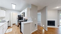This single-floor residence offers a well-organized layout with a neutral color palette of soft grays and warm whites throughout. The entry opens directly to the kitchen, which features white cabinetry, light countertops, a double stainless steel sink positioned beneath a window, and black appliances including a gas range with over-the-range microwave. A peninsula counter with a breakfast bar creates a natural divide between the kitchen and the main living area, while a skylight overhead brings in additional natural light.

The living room is a standout space, highlighted by a tile-surround fireplace and a sliding glass door that opens to an outdoor patio, allowing for natural light and outdoor views. Warm-toned hardwood-style flooring runs throughout the main living and kitchen areas, contributing to a cohesive and inviting atmosphere. A ceiling fan adds both function and style.

The bedrooms are finished with plush carpeting and feature mirrored sliding closet doors that enhance the sense of space. One carpeted room also includes its own sliding glass door to the exterior. The bathroom is neatly appointed with white vanity cabinetry, a tub-shower combination, and wood-look flooring. Textured ceilings are consistent throughout the unit.