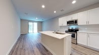 This contemporary two-floor residence is designed with a clean, modern aesthetic that emphasizes open living and functional design throughout. The heart of the home is an open-concept kitchen and living area, where light-toned wood-look flooring extends seamlessly across the space, enhancing the sense of openness and continuity. The kitchen is outfitted with crisp white shaker-style cabinetry, light quartz countertops, and a full suite of stainless steel appliances, including a refrigerator with ice and water dispenser, an electric range, and a built-in microwave. A generously sized center island with an integrated sink serves as both a prep area and a casual gathering point, anchoring the open layout. Recessed lighting illuminates the space evenly, complemented by natural light filtering in through a sliding glass door fitted with vertical blinds. The living area offers an expansive, versatile footprint ideal for a variety of furniture arrangements. The bedrooms are well-proportioned, featuring walk-in closet space and continued wood-look flooring. The bathrooms are finished with white subway tile, including a tub-shower combination and a separate walk-in shower, paired with white vanity cabinetry and brushed nickel hardware. Throughout the residence, neutral tones and consistent finishes create a cohesive, move-in-ready environment.