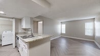 This single-floor residence offers a clean, modern interior finished with a consistent neutral color palette and distinctive herringbone-pattern luxury vinyl flooring that extends throughout the living areas, bedrooms, and hallways. The open-concept layout connects the living room to the kitchen, which is anchored by a granite-topped peninsula with an undermount sink — an ideal space for both meal preparation and casual dining. White cabinetry, stainless steel appliances, and recessed lighting give the kitchen a polished, functional character. The living area is generously proportioned, receiving natural light through window blinds that line the exterior walls. The bedrooms are well-sized, each featuring the same herringbone flooring, ceiling fans with lighting, and windows that invite natural light. The bathroom is outfitted with a granite vanity top, white cabinetry, a framed mirror, and a shower-tub combination, maintaining the home's cohesive aesthetic. A dedicated in-unit laundry area with a full-size washer and dryer adds everyday convenience. Textured ceilings and clean white baseboards complete the interior, contributing to a tidy, move-in-ready atmosphere throughout this thoughtfully designed single-level home.