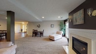 Located at 815 Cole Dr in Johnstown, Ohio, this single-floor property offers a well-organized layout with distinct living, dining, and kitchen areas. The spacious main living room is anchored by a classic gas fireplace framed by a white decorative mantel, set against a bold dark accent wall adorned with wall sconces and artwork. Plush carpeting extends throughout the living area, creating a warm and comfortable atmosphere. Natural light filters in through French doors, which also provide a view to the exterior. A chaise lounge and open floor plan give the living space a relaxed, functional feel. Adjacent to the living room, a dining area features wood-look tile flooring and accommodates a dark wood dining table with chairs. This flooring continues into the entry foyer, where sidelights flank the front door and provide additional natural light. The kitchen is practical and efficient, offering cabinetry, a countertop with an integrated sink, wood-look tile floors, a refrigerator, microwave, and built-in shelving for storage and organization. A textured ceiling is consistent throughout the space, and recessed lighting provides even illumination across all areas. The layout flows cohesively from room to room, making this a functional and inviting single-level property.