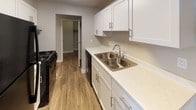 This 2-bedroom, 1-bathroom unit is thoughtfully laid out across a single floor, offering a comfortable and functional living environment. The open living area features a combination of durable hardwood-style flooring and plush carpet, a ceiling fan for added comfort, and a large window dressed with vertical blinds that invites natural light throughout the space. Baseboard heating is present throughout, ensuring consistent warmth. The kitchen is well-appointed with white shaker-style cabinetry, light countertops, a double-basin stainless steel sink, and black appliances including a gas range and dishwasher. Hardwood-style flooring continues through the kitchen, which also provides access to a dedicated storage or pantry area. Both bedrooms are carpeted and generously sized, with neutral gray walls and textured ceilings. The primary bedroom features an expansive wall of louvered bi-fold closet doors, offering excellent storage capacity. The second bedroom includes a window with natural light and a wall-mounted AC unit. The full bathroom is finished with tile flooring, a wide vanity with light countertops and white cabinetry, a large mirror, and a full tub-shower combination, completing this well-rounded and move-in-ready home.