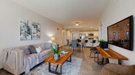 Located along North Tamiami Trail in Sarasota, Florida, this single-floor residence offers a thoughtfully designed open-concept layout that seamlessly connects the kitchen, dining, and living areas. The kitchen is outfitted with white shaker cabinetry, a quartz-topped island with seating, stainless steel appliances including a French door refrigerator, and recessed lighting — providing both functionality and a clean aesthetic. The open dining area flows naturally into a spacious living room bathed in natural light from large windows, complemented by neutral tile flooring that runs consistently throughout the unit. The primary bedroom features a tray ceiling, sliding glass doors opening to a private outdoor area, and direct access to a well-appointed bathroom with a glass-enclosed shower, white vanity with quartz countertop, and stone-look tile flooring. A second bedroom offers comfortable proportions and closet access. A dedicated laundry area with a full-size washer and dryer adds everyday convenience. The overall design palette of soft whites, warm neutrals, and modern fixtures creates a bright, cohesive ambiance suited to Florida living.