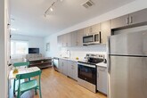 Unit 602 at 1 East Main Street in Bound Brook, NJ offers a thoughtfully designed one-bedroom, one-bathroom residence with a contemporary aesthetic and efficient use of space. The open-plan living area seamlessly integrates the kitchen, dining, and living zones, creating a bright and cohesive environment bathed in natural light from large windows. Light hardwood flooring flows throughout the unit, enhancing the airy feel.

The kitchen is well-appointed with sleek grey flat-front cabinetry, a distinctive white hexagonal tile backsplash, and a full suite of stainless steel appliances including a refrigerator, electric range, microwave, and dishwasher. A dining area adjacent to the kitchen provides a functional space for everyday meals. The living area offers a comfortable retreat with access to a large window overlooking the surroundings.

The bedroom is a calm, light-filled space featuring a wide window with horizontal blinds and ample room for a full furniture arrangement. A dedicated closet provides practical storage. The bathroom is finished in a clean, minimalist style with white tile flooring, a grey vanity with a stone-topped sink, a mirror, and chrome fixtures. Track lighting throughout the main living area adds a modern design touch, rounding out this well-appointed urban residence.
