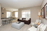This thoughtfully designed single-floor residence offers a comfortable and functional layout across a generous footprint. The living room serves as the heart of the home, featuring plush carpeting, a large window fitted with horizontal blinds that allows abundant natural light, and neutral taupe walls that create a warm, inviting ambiance. Framed wall art and a textured ceiling add character to the space.

The dining area accommodates a high-top table with bench seating, flanked by two windows overlooking the outdoors, making it an ideal spot for casual meals. The kitchen is outfitted with light maple cabinetry, dark granite-style countertops, hardwood flooring, and black appliances including a range and built-in microwave, offering both style and practicality.

The primary bedroom is a serene retreat with soft carpeting, a ceiling fan, and direct access to a spacious walk-in closet featuring built-in shelving and hanging rods. Its en-suite bathroom includes a glass-enclosed shower, a vanity with dark countertops, and tile flooring. A second bedroom also features carpeting and warm lighting, with an adjacent full bathroom complete with a tub-shower combination, tile surround, and matching dark-countered vanity.