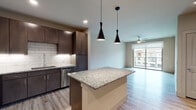 This single-story, one-bedroom, one-bathroom residence is designed with a contemporary open-concept layout that seamlessly connects the kitchen, dining, and living areas. Light wood-style flooring flows throughout, lending a clean and cohesive aesthetic across the space.

The kitchen is a standout feature, anchored by a generous granite-topped island with pendant lighting overhead. Dark espresso cabinetry extends to the ceiling, providing ample storage, while a classic white subway tile backsplash offers crisp contrast. Stainless steel appliances—including a French door refrigerator, electric range, over-the-range microwave, and dishwasher—complete the well-equipped space.

The living area is bright and airy, benefiting from a ceiling fan and a full-width sliding glass door that opens to a private balcony, allowing natural light to fill the room and offering views of the surrounding community.

The bedroom continues the light flooring and includes its own sliding glass door access to the balcony, along with a ceiling fan for added comfort. The bathroom features tile-surround tub and shower combination and direct access to a walk-in closet with built-in shelving, providing practical and organized storage.