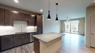 This single-story, one-bedroom, one-bathroom residence is designed with a contemporary open-concept layout that seamlessly connects the kitchen, dining, and living areas. Light wood-style flooring flows throughout, lending a clean and cohesive aesthetic across the space.

The kitchen is a standout feature, anchored by a generous granite-topped island with pendant lighting overhead. Dark espresso cabinetry extends to the ceiling, providing ample storage, while a classic white subway tile backsplash offers crisp contrast. Stainless steel appliances—including a French door refrigerator, electric range, over-the-range microwave, and dishwasher—complete the well-equipped space.

The living area is bright and airy, benefiting from a ceiling fan and a full-width sliding glass door that opens to a private balcony, allowing natural light to fill the room and offering views of the surrounding community.

The bedroom continues the light flooring and includes its own sliding glass door access to the balcony, along with a ceiling fan for added comfort. The bathroom features tile-surround tub and shower combination and direct access to a walk-in closet with built-in shelving, providing practical and organized storage.